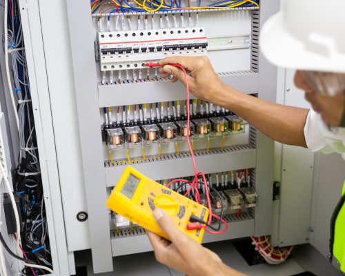 Electrician engineer work tester measuring voltage and current of power electric line in electical cabinet control.