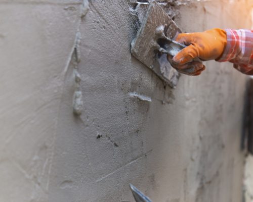 The hands of a worker who are plastering up close are wearing orange rubber gloves to prevent the cement from biting their hands, building the house walls and having beautiful orange lights.